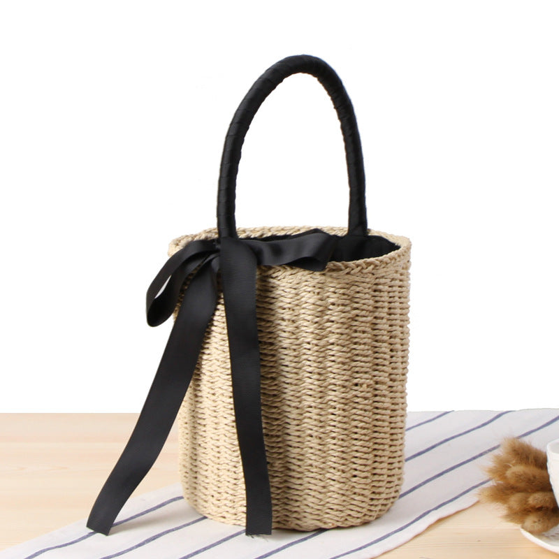 Woven basket with black handle and ribbon on a striped surface