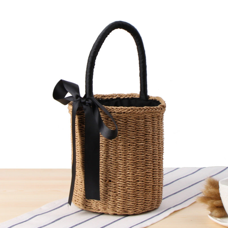 Woven basket with a black handle and ribbon on a striped surface