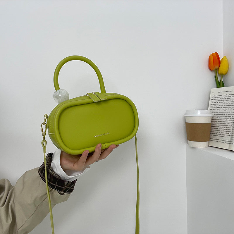 Person holding a green handbag with a white wall and coffee cup in the background