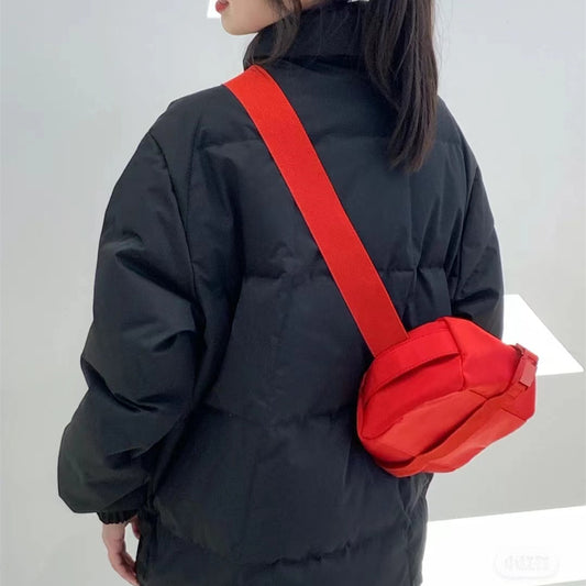 Person wearing a black coat with a red crossbody bag on a plain background