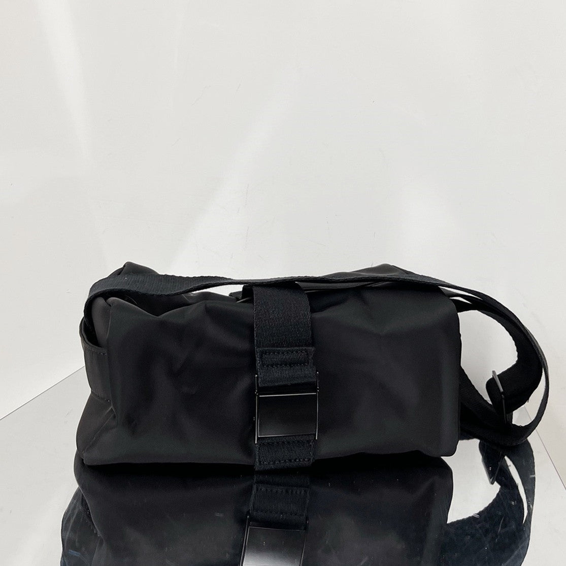 Black bag with a strap on a reflective surface and light gray background