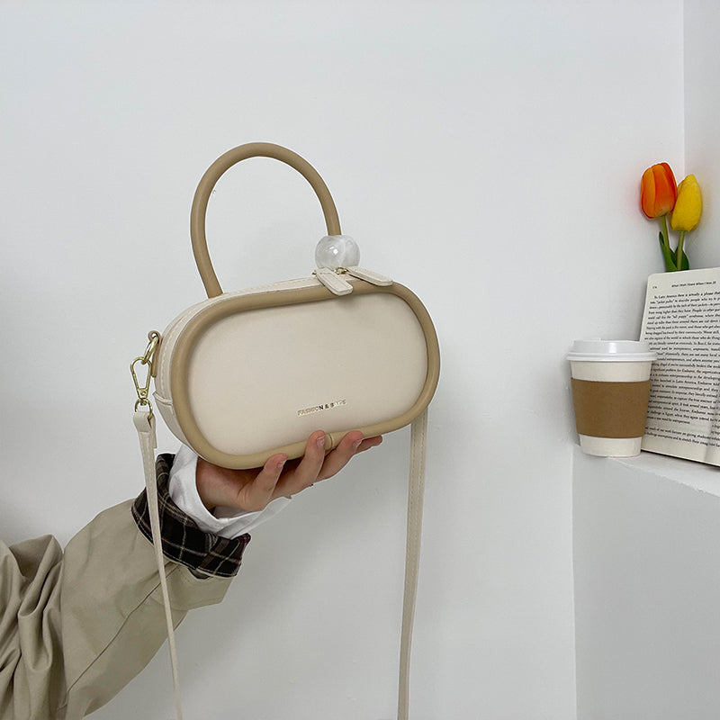 Beige handbag held by a person against a white wall with a cup and tulips in the background.