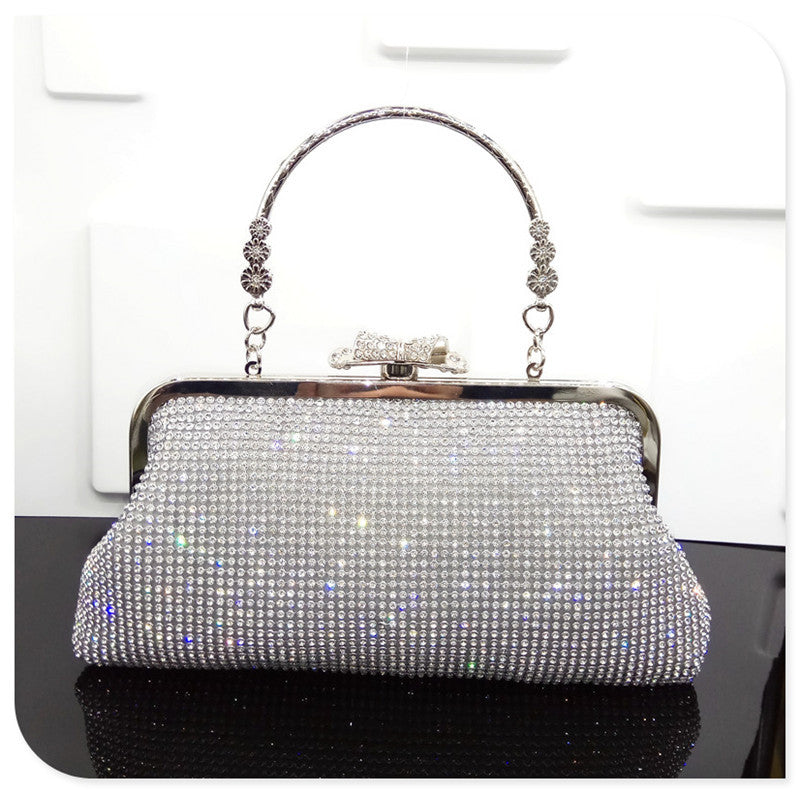 Silver clutch bag with rhinestone embellishments on a reflective surface.