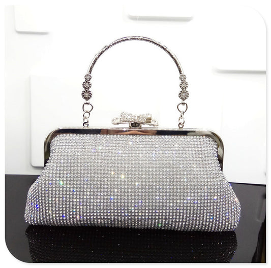 Silver clutch bag with rhinestone embellishments on a reflective surface.