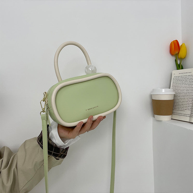 Person holding a green and beige handbag against a white wall with a cup and tulips in the background.