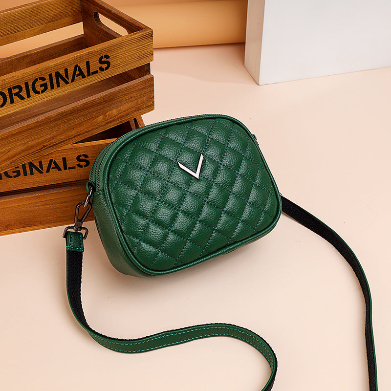 Green quilted handbag with a brand logo on a beige surface, with wooden crates in the background.